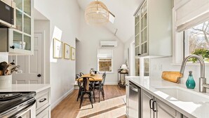 A modern kitchen with white cabinetry, a dining area with a wooden table and chairs, and a large window providing natural light. - Walk To Town - Beautiful Edgartown House  (Edgartown)