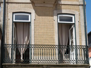 A building facade with two windows, a patterned wall, and a balcony with a metal railing.