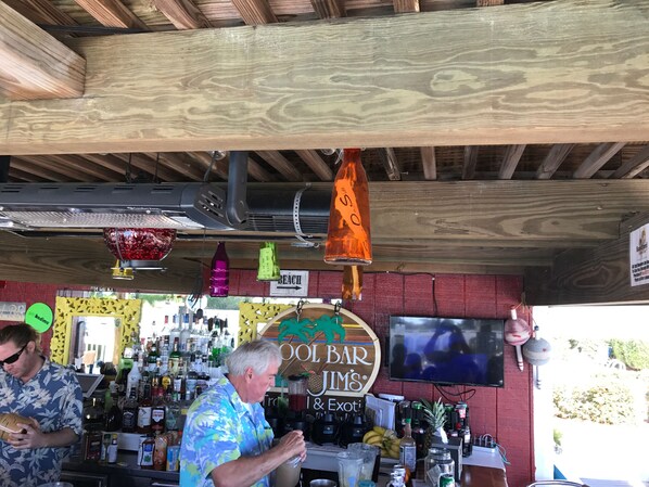 Un bar con vigas de madera en el techo, luces colgantes y un letrero que dice "COOL BAR JIM'S".