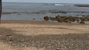 Een strand met een rotsachtige kustlijn en een rustige zee.