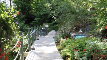 A wooden pathway leading to a pool area surrounded by lush greenery and flowering plants.