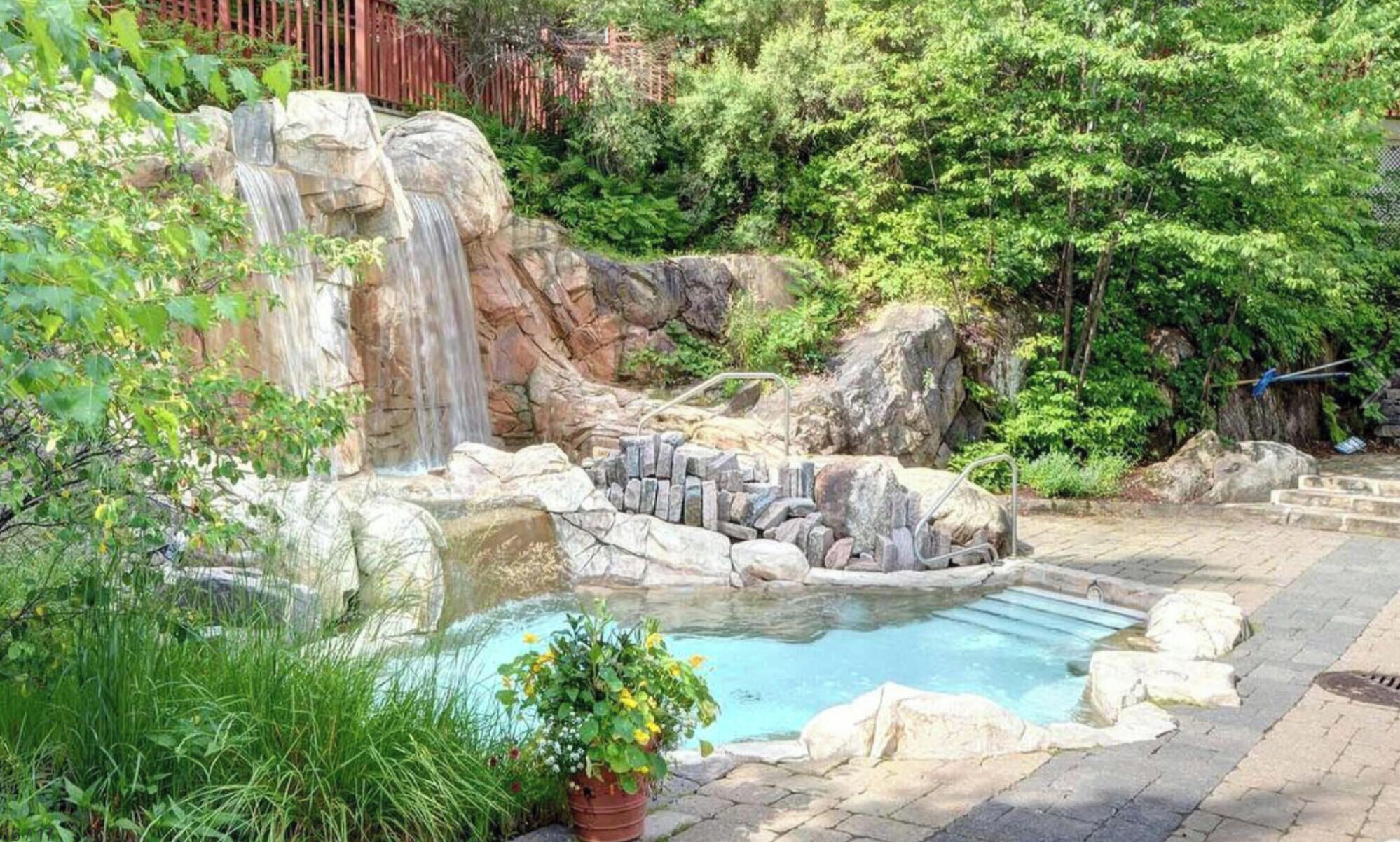 A natural pool with a waterfall, surrounded by rocks and greenery.