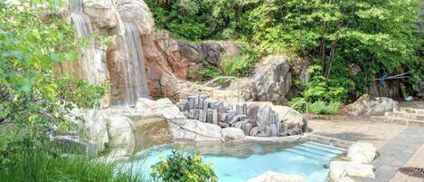 A natural pool with a waterfall, surrounded by rocks and greenery.