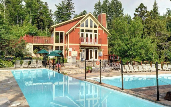 A two-story building with a pool, surrounded by trees.