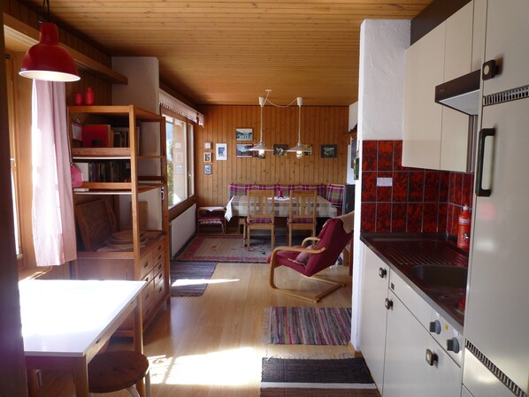 Un interno accogliente di una baita con zona pranzo, una poltrona rossa e una cucina con frigorifero.