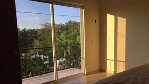 A bedroom with a large sliding glass door leading to a balcony with a view of greenery and a body of water. - 2BED/2BA, Pool, Lush Gardens, Private Rooftop, Walk to Beach & Downtown (Bucerías)