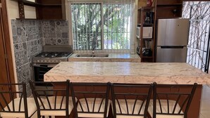 A kitchen with a large island, a stove, and a refrigerator. - 2BED/2BA, Pool, Lush Gardens, Private Rooftop, Walk to Beach & Downtown (Bucerías)