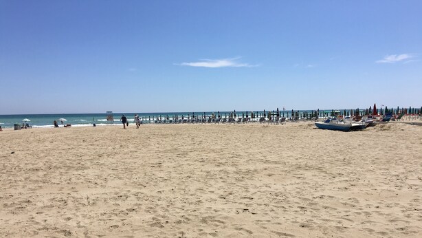 A beach with rows of umbrellas and lounge chairs, a pier in the background, and a clear sky. - Air conditioned, brand new mini loft apartment first row sea (Tortoreto Lido)