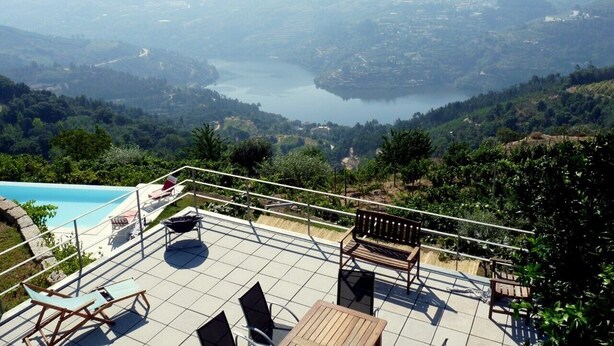 Una terraza con piscina, mobiliario exterior y vistas a un lago y montañas.