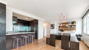 A modern kitchen with a central island, bar stools, and a dining area with a dark wood table and chairs. - St Kilda Penthouse with Panaromic Bay and City View (St Kilda West)