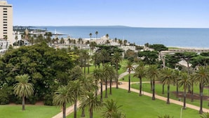 A coastal view with a park, palm trees, and a building in the background. - St Kilda Penthouse with Panaromic Bay and City View (St Kilda West)