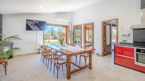 Een ruime keuken met een groot eiland, een eethoek met een lange tafel en stoelen, en uitzicht op de omgeving door grote ramen.