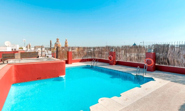 A rooftop pool with a clear view of the city skyline, including distinctive buildings and a barbed wire fence.