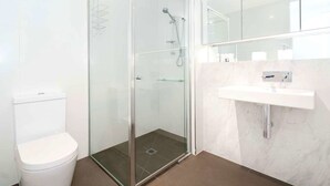 A modern bathroom with a glass-enclosed shower, a white toilet, and a marble sink. - Broadway in Elwood on the Canal (Elwood)