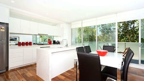 A modern kitchen with a central island, white cabinetry, and a dining area with black chairs and a red bowl. - Broadway in Elwood on the Canal (Elwood)