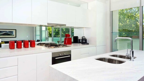 A modern kitchen with white cabinetry, a stainless steel sink, and a coffee maker. - Broadway in Elwood on the Canal (Elwood)