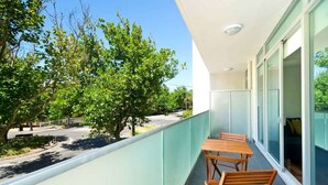 A balcony with a table and chairs, overlooking a road and trees. - Broadway in Elwood on the Canal (Elwood)