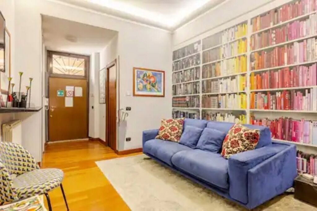 A room with a blue sofa, a patterned chair, and a bookshelf filled with books.