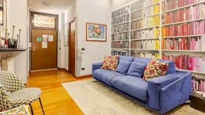 Une pièce avec un canapé bleu, un fauteuil à motifs et une bibliothèque remplie de livres.