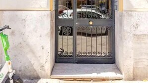 Une entrée d’immeuble avec une arche jaune, un portail en métal noir et un scooter vert garé à l’extérieur.