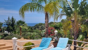 Two white lounge chairs with blue cushions on a patio with a view of the sea and surrounding greenery. - Santa Eulalia Del Rio: chalet - IbizaHouse with character with pool and bbq place and magic seaview (santa eulalia del rio)