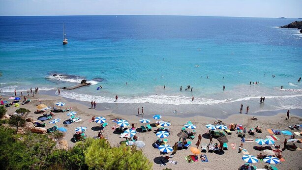 A beach with clear blue water, people swimming, and umbrellas. - Santa Eulalia Del Rio: chalet - IbizaHouse with character with pool and bbq place and magic seaview (santa eulalia del rio)