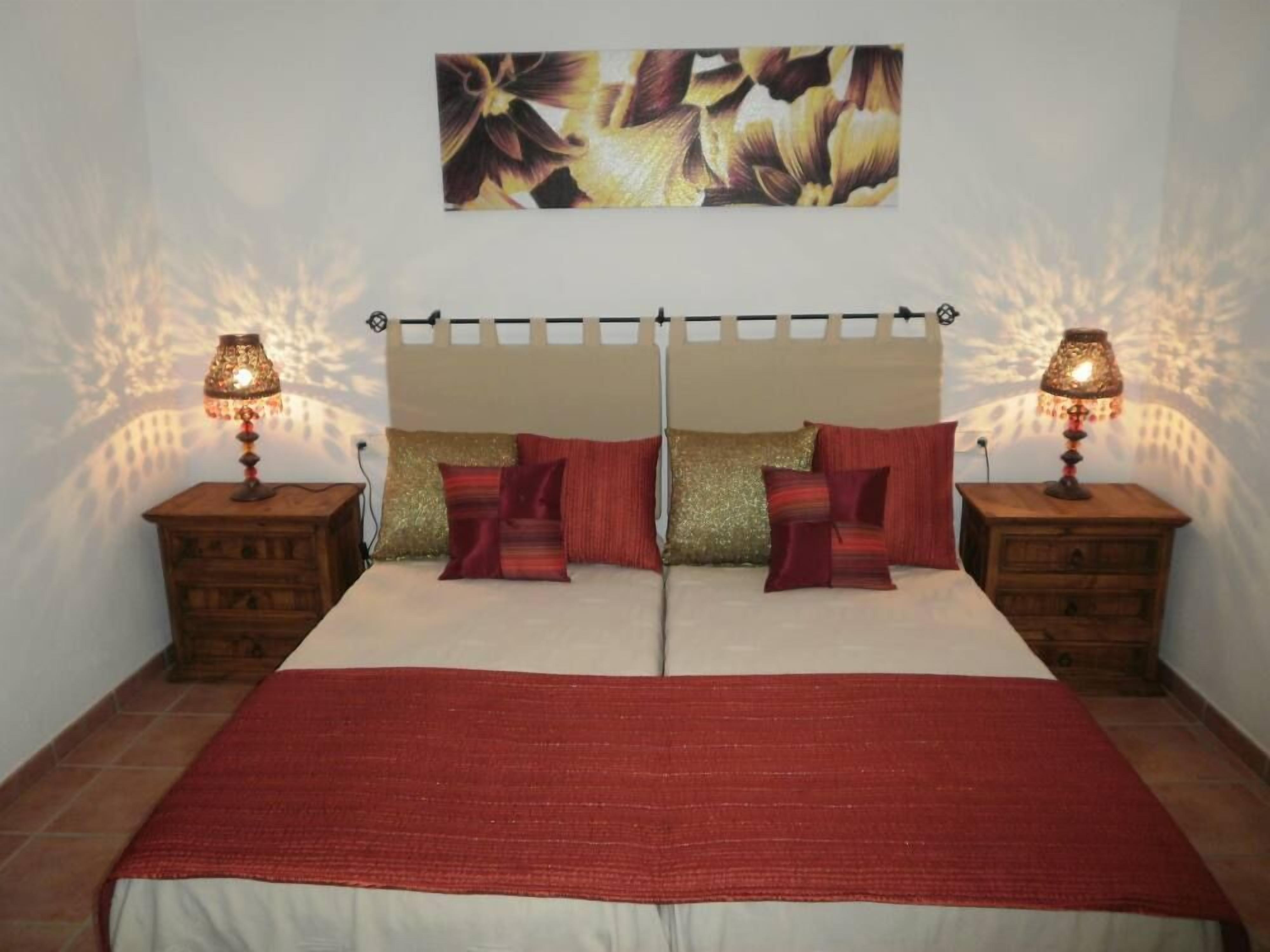 A double bed with a red blanket, two nightstands with lamps, and a floral artwork above the bed.