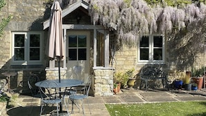 A stone house with a garden patio, a covered seating area, and a view of the surrounding landscape.