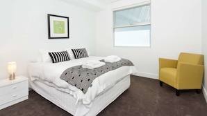 Una camera da letto con un letto, un comodino, una sedia, una finestra e un quadro appeso al muro.