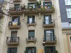 A multi-story building with balconies, some with plants and flags.