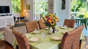 A dining area with wicker chairs, a table set with plates, and a vase of flowers. - Lovely 2 bed/2bath apartment, 10 mins to Hastings beach, a/c, veranda, garden (Bridgetown)
