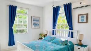A bedroom with a bed, curtains, a window, a picture frame, and a nightstand. - Lovely 2 bed/2bath apartment, 10 mins to Hastings beach, a/c, veranda, garden (Bridgetown)