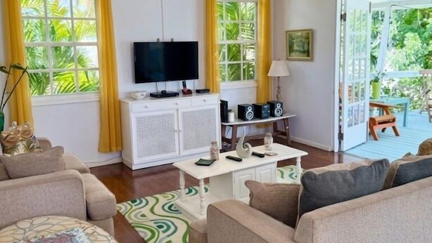 A living room with a television, sofa, coffee table, and a ceiling fan. - Lovely 2 bed/2bath apartment, 10 mins to Hastings beach, a/c, veranda, garden (Bridgetown)