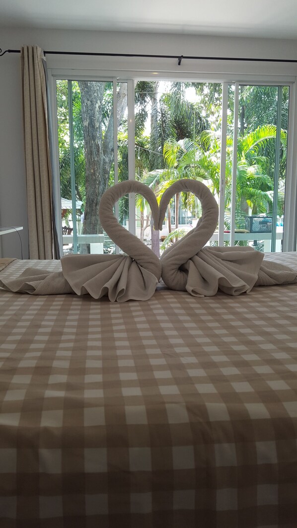 A hotel room with a bed, a window with curtains, and a view of greenery outside.