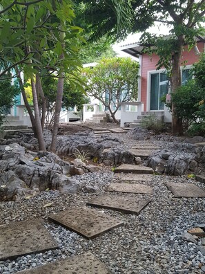 A garden area with stone pathways, trees, and a building in the background.