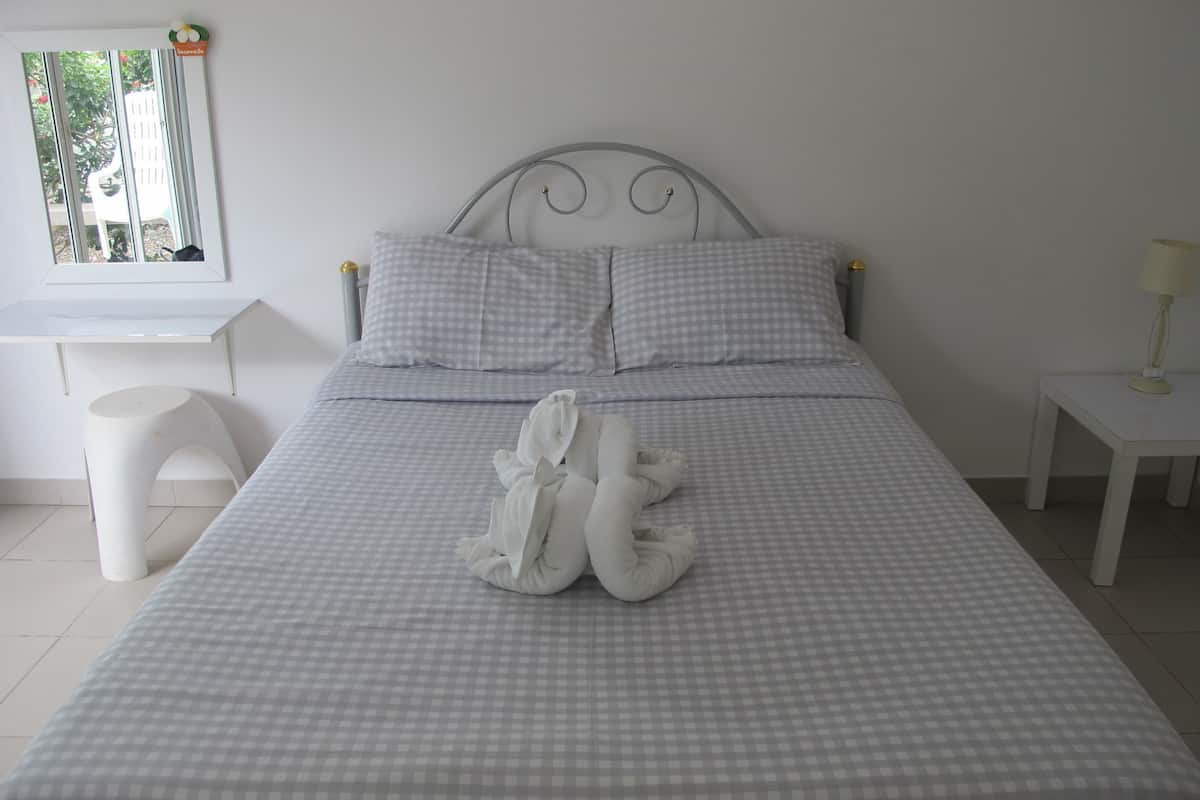 Uma cama bem arrumada com colcha xadrez, cabeceira branca e uma pequena mesa de cabeceira com abajur.