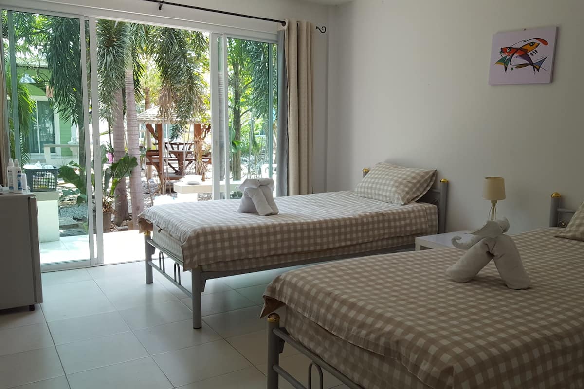 Quarto de hotel com duas camas, uma varanda e vista para palmeiras, e um quadro na parede.