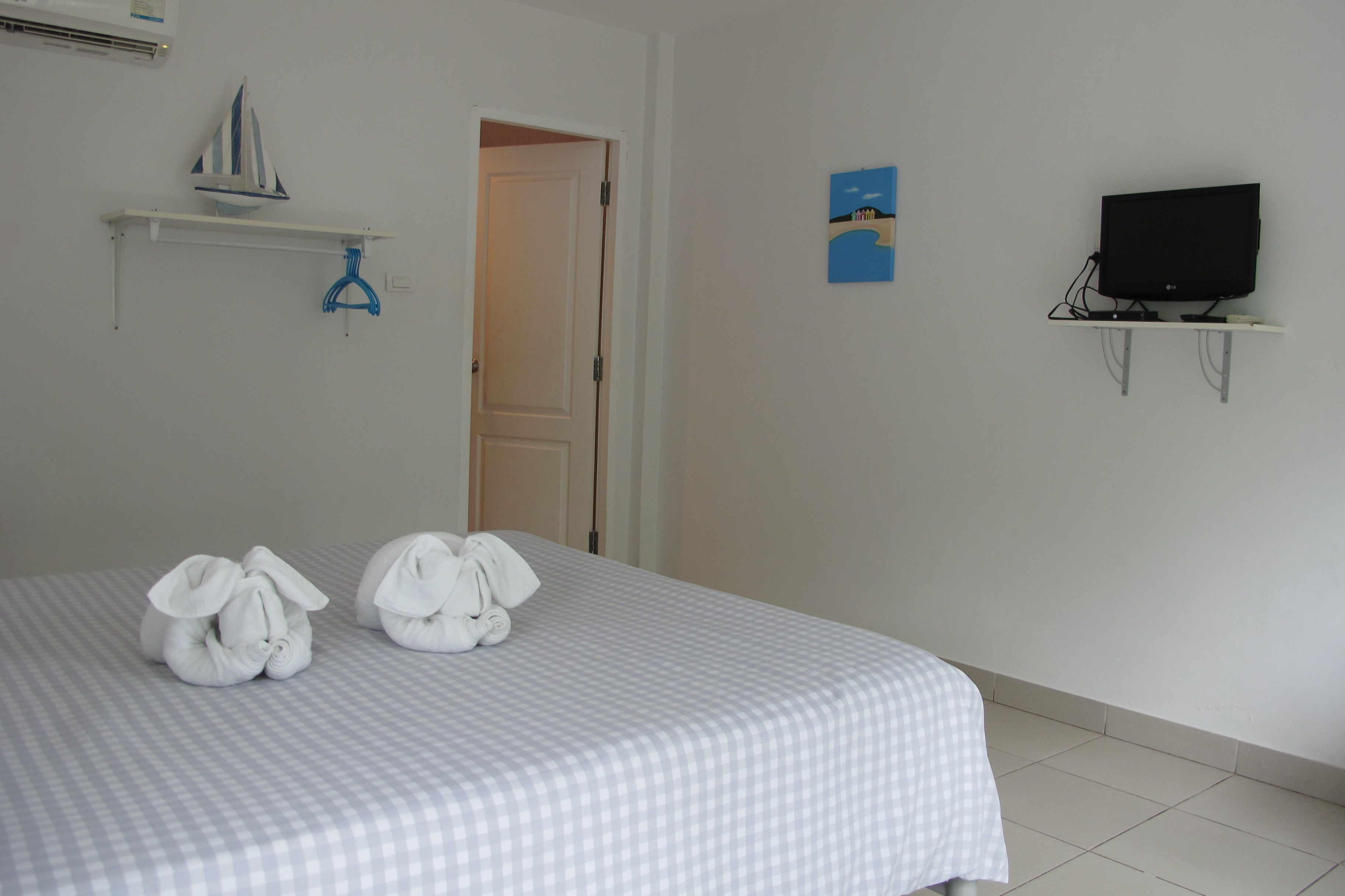 A hotel room with a bed, a television on a stand, and a door leading to another room.