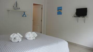A hotel room with a bed, a television on a stand, and a door leading to another room.