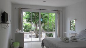 Un dormitorio con cama, escritorio, televisor y vista a espacios verdes al exterior.