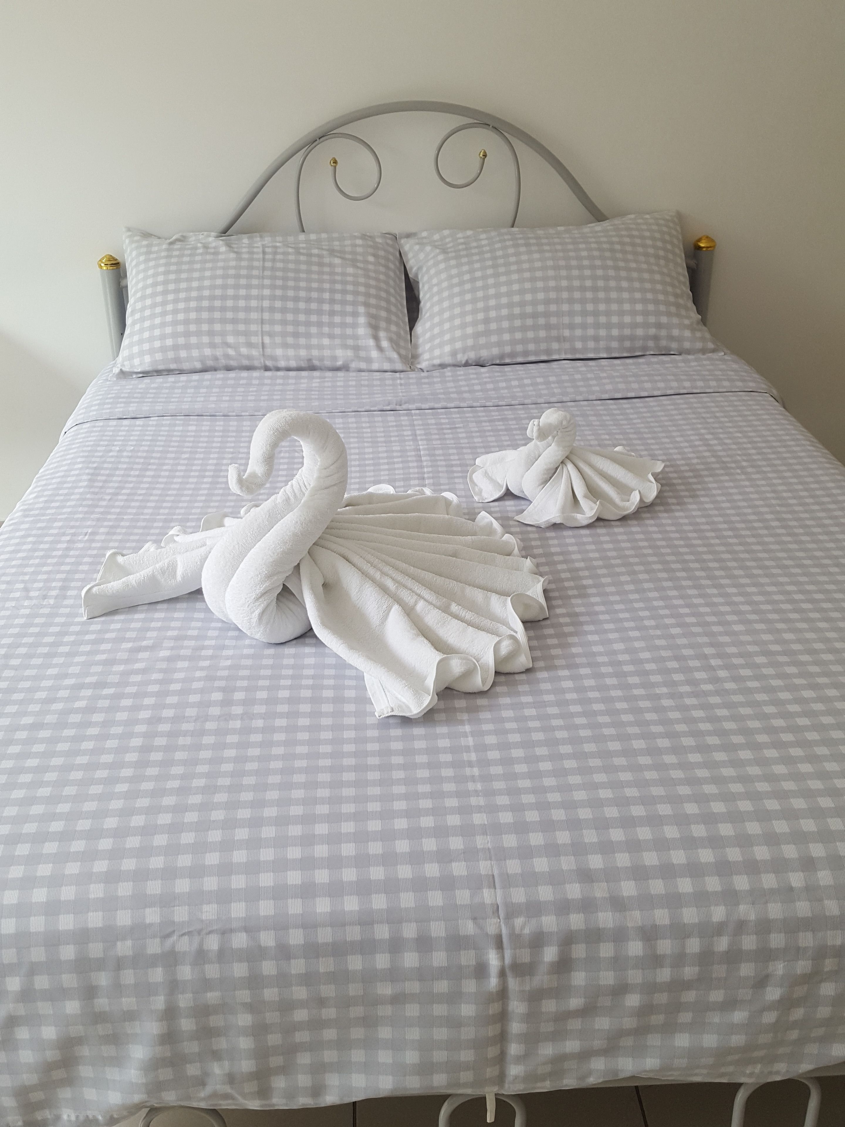A neatly made bed with a checkered bedspread and two swan-shaped towels.