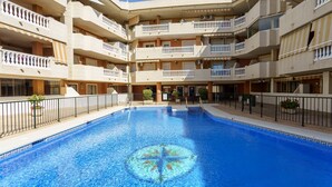 A multi-story hotel with a central swimming pool, balconies on each floor, and a clear blue sky.