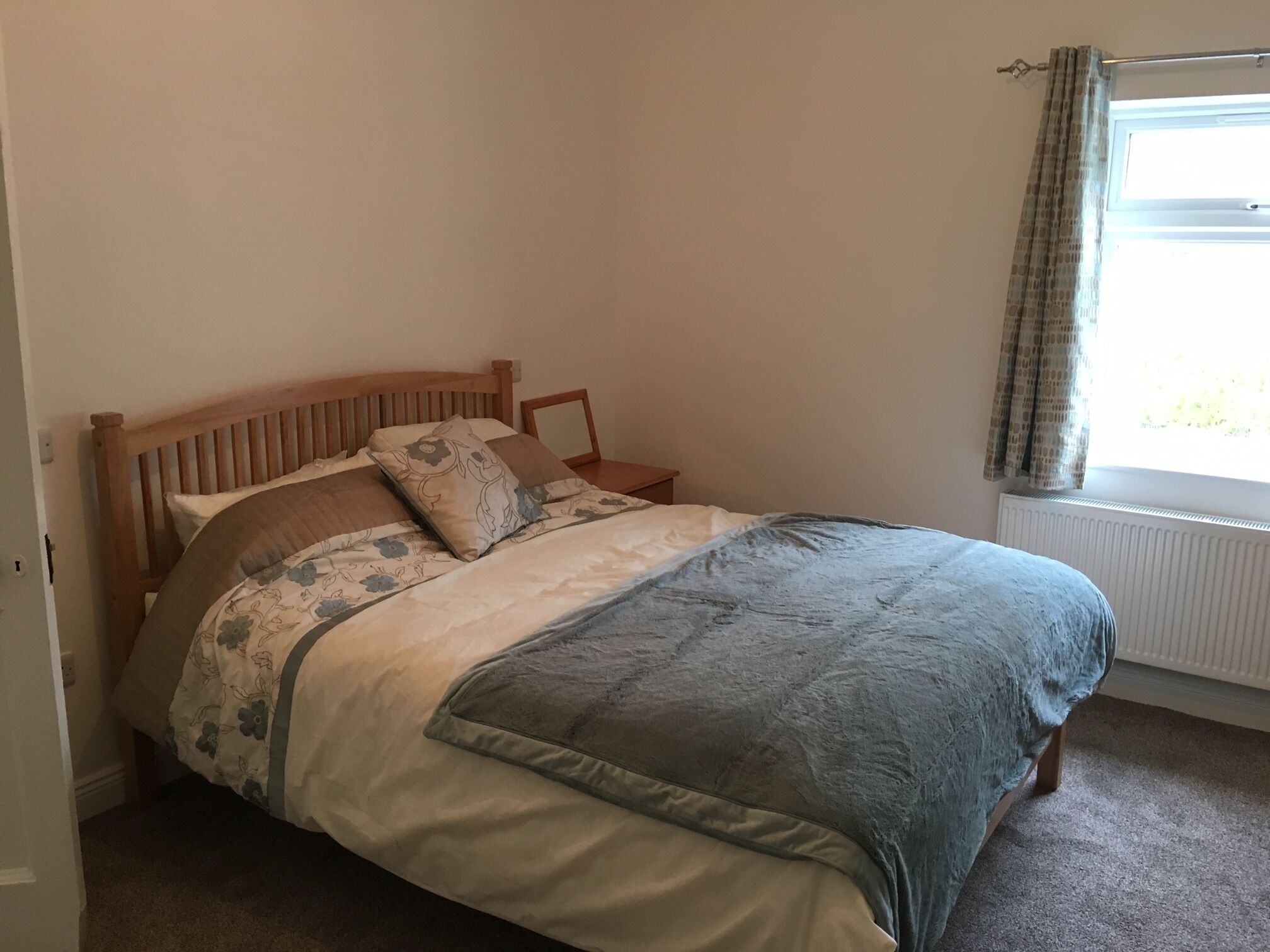 A bedroom with a wooden bed, floral bedding, a grey blanket, and a window with curtains.