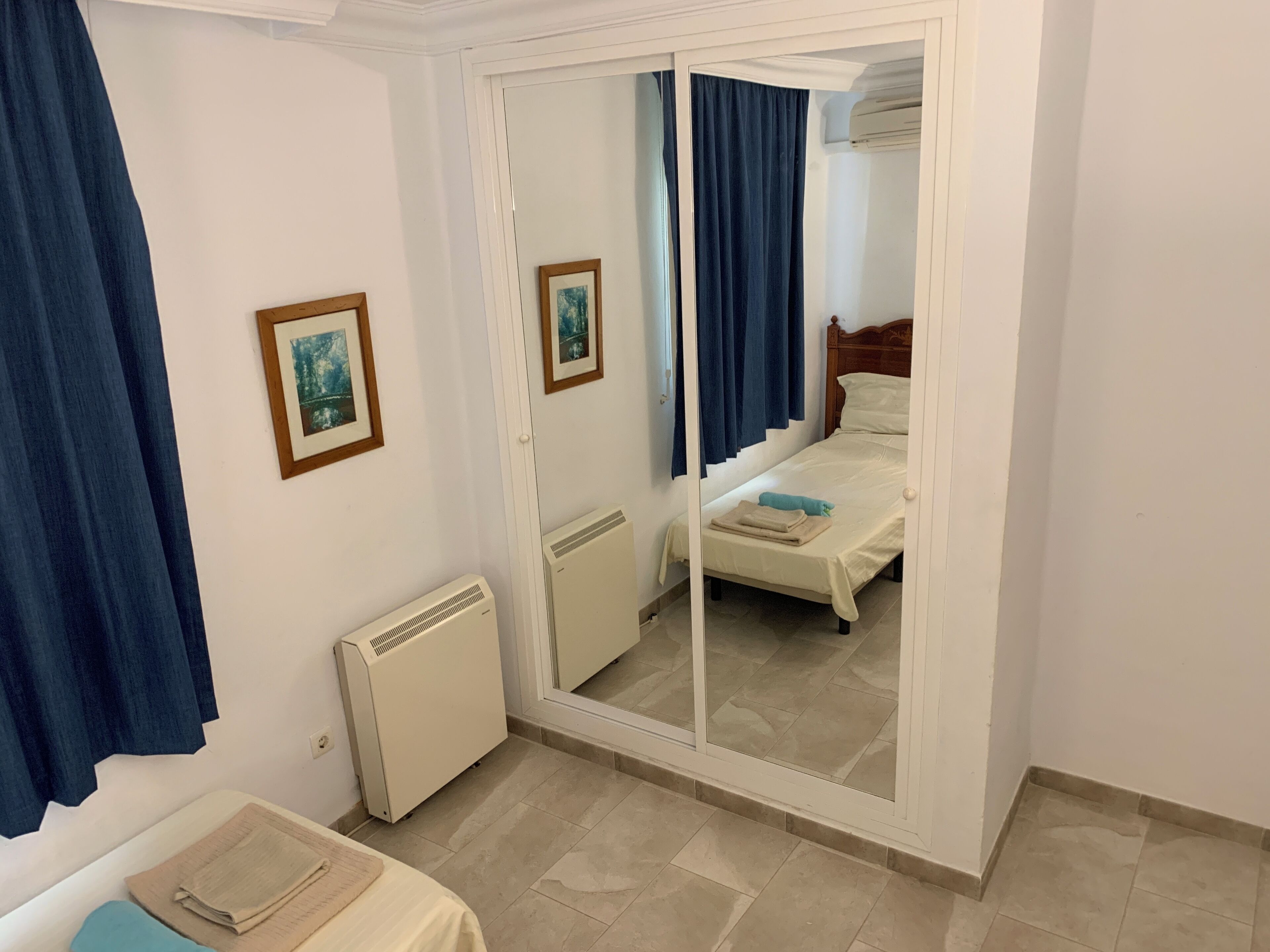 A hotel room with a bed, a radiator, a mirror, and a door leading to another room.