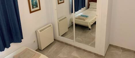 A hotel room with a bed, a radiator, a mirror, and a door leading to another room.