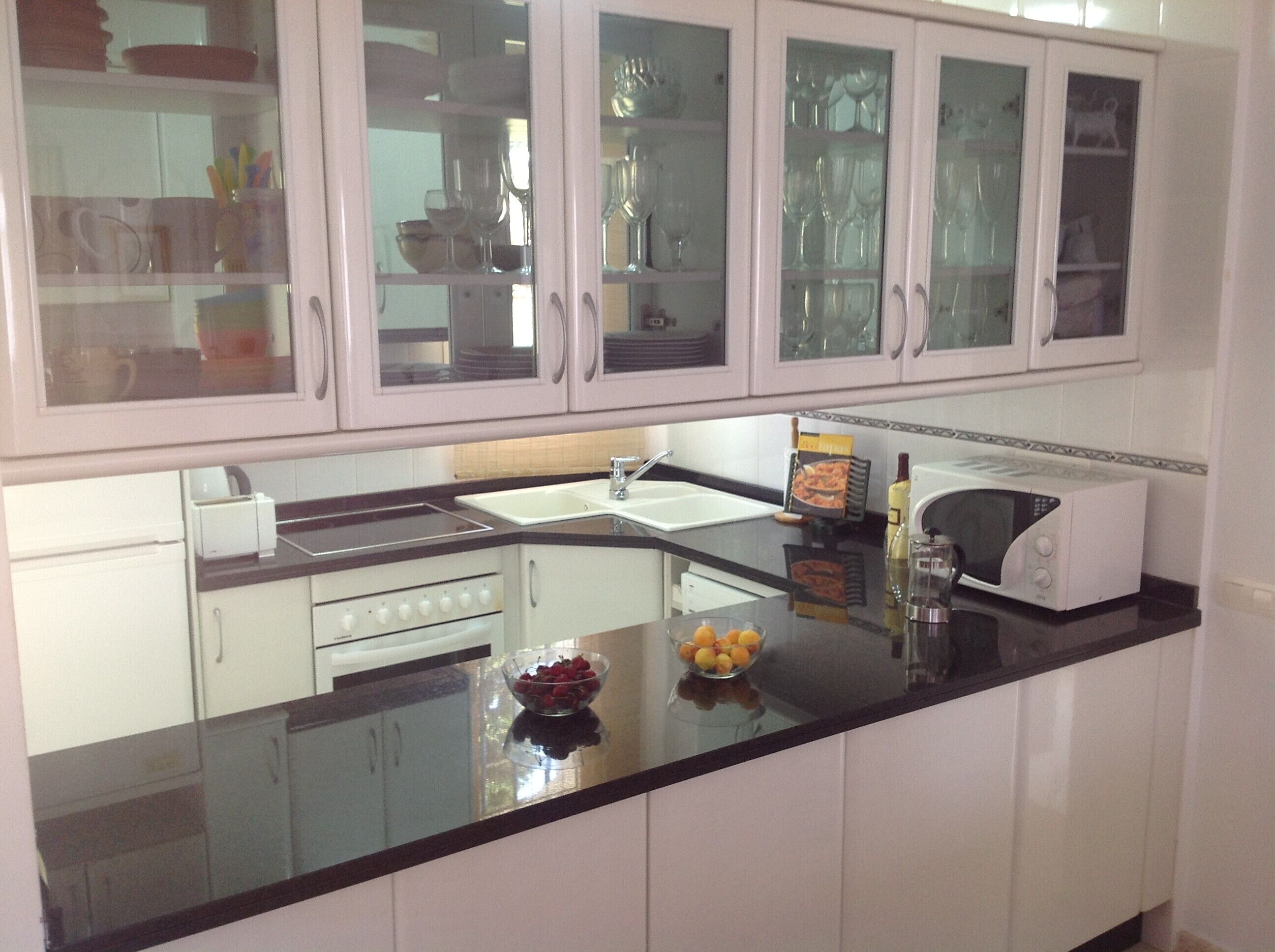 A kitchen with white cabinets, a black countertop, a microwave, a sink, and a bowl of fruit.