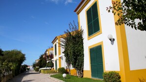 A cobblestone street lined with yellow buildings with green shutters. - Villa located in the last condo before arriving the beach of Meco (Sesimbta)