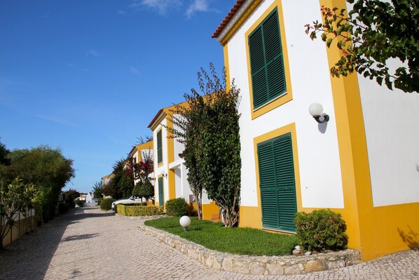 A cobblestone street lined with yellow buildings with green shutters.