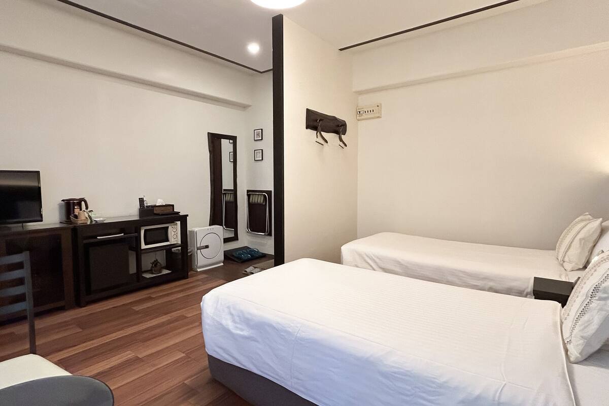 Habitación de hotel con dos camas individuales, un televisor, un escritorio con microondas y una silla.