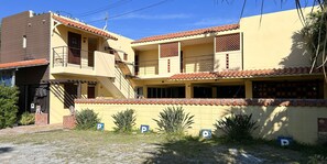 A two-story building with a yellow facade, red-tiled roof, and a small balcony. There are three parking spaces marked with 'P' signs. - Pension Sunset Beach (Nakijin)
